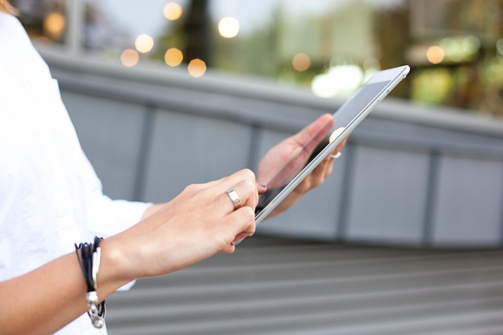 Woman standing outside holding a tablet in her left hand and scrolling with her right hand.